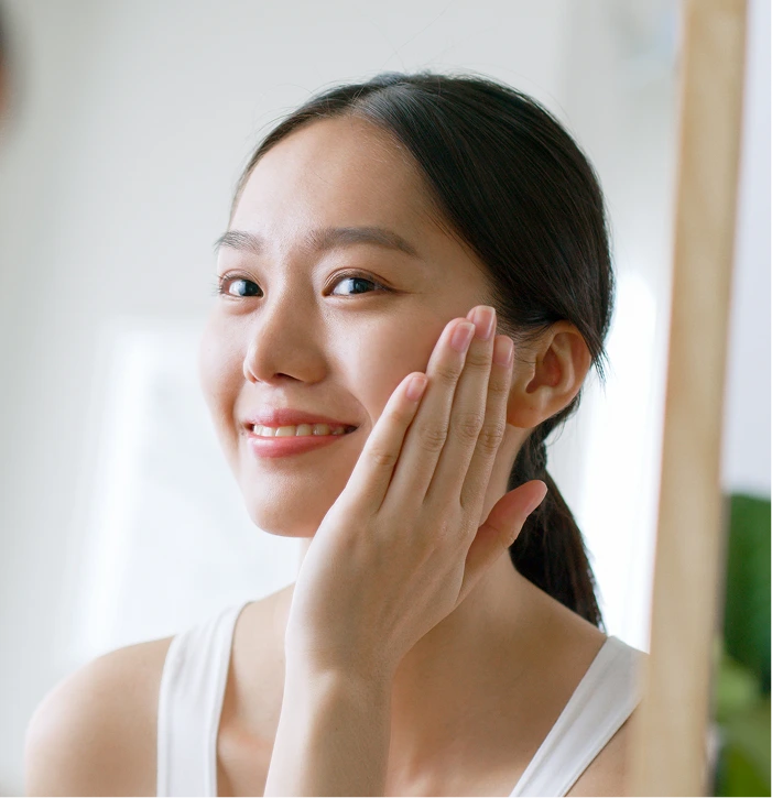 Woman touching her cheek and smiling, demonstrating healthy skin